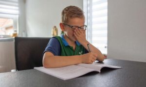 jongen met werkschrift aan tafel hand voor mond