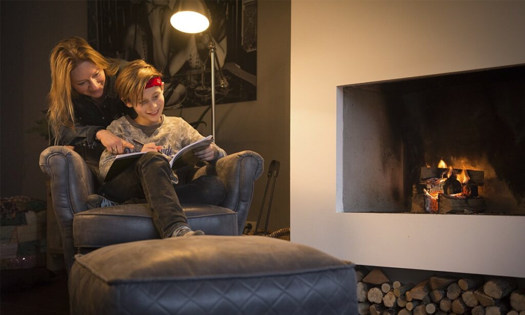 moeder helpt zoon met oefeningen in werkboek bij de open haard