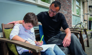 jongen en vader zitten buiten in de zon op een bankje en maken huiswerk