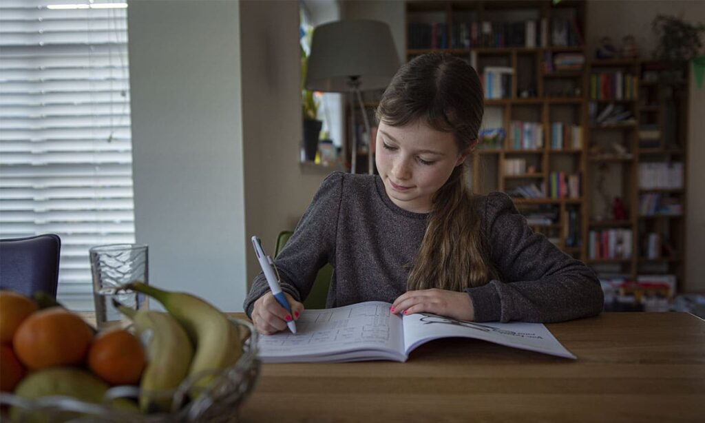 meisje zit aan tafel met werkboek