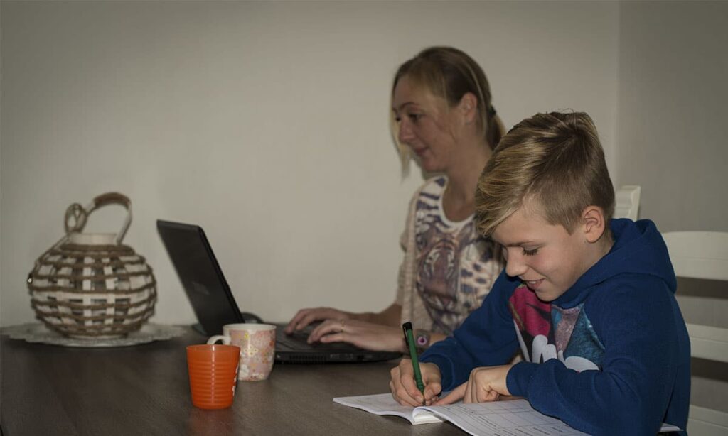 moeder werkt aan laptop en zoon maakt opdrachten in werkboek