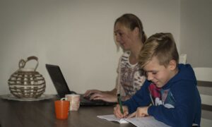 moeder werkt aan laptop en zoon maakt opdrachten in werkboek