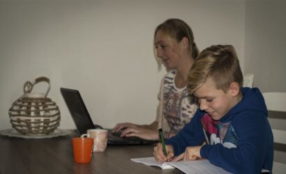 moeder werkt aan laptop en zoon maakt opdrachten in werkboek