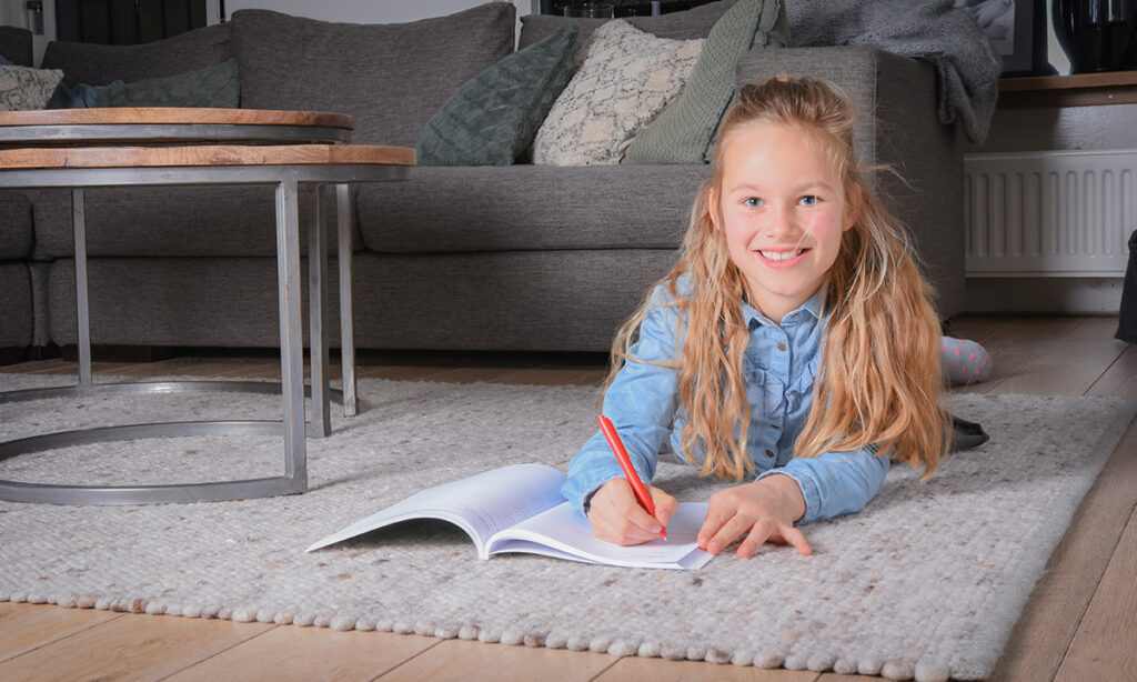 meisje op vloerkleed maakt opdrachten in boek